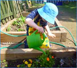 image of child with watering can in outdoor area watering plants